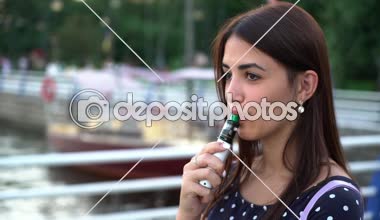 Neşeli kız e-sigara ile Yatlar ayakta ve güzel günbatımı üzerinde bir nehir dolgu yat ile elektronik sigara sigara gülümseyen güzel bir kızın muhteşem günbatımı A neşeli manzaraya bir nehir iskele üzerinde