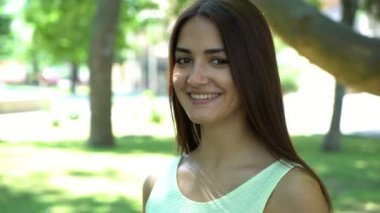 Komik kız gülümsüyor neşeli bir yeşil park sokaktaki güneşli bir günde mutlu yaz aylarında güneşli ve yeşil çimenler ile dar bir sokakta gülümseyen bir beyaz kolsuz elbise komik bir şık genç kadın portresi