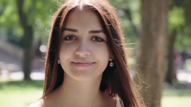 Güzel kız gülümsüyor romantik mutlu bir arka sokakta yapraklı ağaçlar ve güneşli çayırlar ile yaz aylarında gülümseyen uzun esmer saçlı rüya gibi bir genç kadın portresi güneşli bir yeşil park sokakta