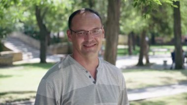 Mutlu adam gözüne gözlük standları ve gülümser bir arka sokakta güneşli bir yaz göz gözlük ve ayakta ve mutlu bir şekilde yaz aylarında eski ağaçlar ve kişiler ile yeşil arka sokakta gülümseyen çizgili bir gömlek neşeli bir adam portresi