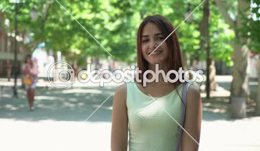 Neşeli genç kadın uzun saçlı gülümsüyor ile mutlu yaz beyaz sleevless neşeli genç bir kadın portresi yeşil bir parkta elbise ayakta ve şefkatle eski ağaçları ile yeşil bir parkta yaz aylarında gülümseyen