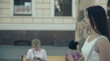 Şık kız yaz profil bir şehir yaz aylarında güneşli bir sokak boyunca strolling beyaz kolsuz elbise içinde zarif bir genç kadın güneşli bir günde bir cadde boyunca yürürken uzun saçlı. O muhteşem görünüyor