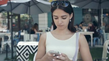 Akıllı ve güzel kız telefonunda bir kafede yaz ekran, onun Smartphone cep telefonu ile mesaj yaz aylarında bir kafeteryada otururken dokunmadan beyaz bir elbise genç güzel bir kadın portresi olmak net sörf