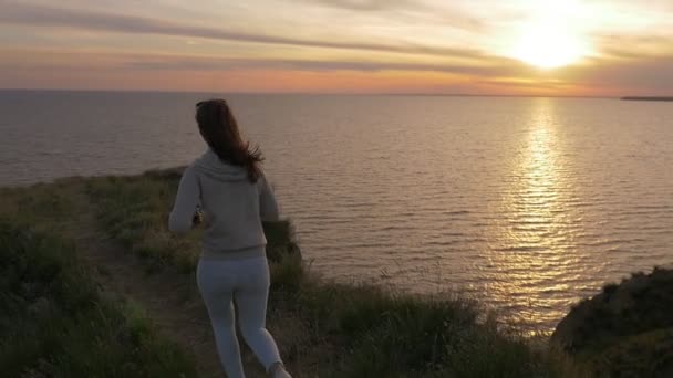穿着运动服的时髦女人在夏天的海边享受灿烂的日落 一个身材修长的年轻女子 长头发看着金色的日落 在黑海海岸上的夏天闪闪发光的阳光路径 — 图库视频影像