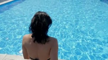 Mutlu kadın ayak ilk atlar slo-mo kristal su ile bir yüzme havuzunda bikini uzun saçlı bir ince kadın ayak ilk açık bir havuzda yavaş güneş ışınları altında oynarken celester suları ile atlar