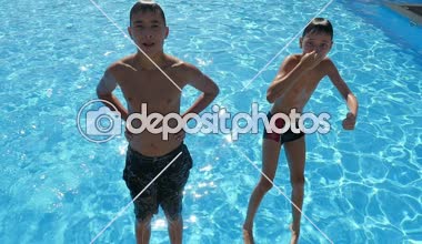 İki erkek zevk için bir yüzme havuzunda slo-mo düşen ve ayak ilk yüzme havuzu gök mavisi suları içine yavaş yaz aylarında güneşli bir atlama iki erkek neşeli bir görünümünü güneşli bir günde düşüyor