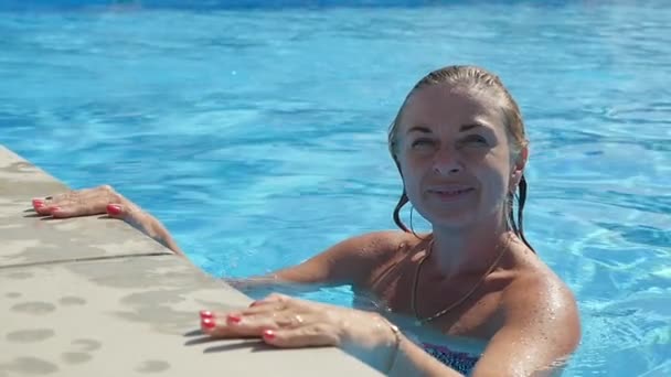 快乐的女人把她的手放在游泳池的边缘 跳在斯洛伐克的肖像 一个活泼的金发女郎微笑着 微微跳在游泳池里 有一双蔚为水 把她的手放在慢动作的边缘上 — 图库视频影像