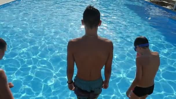 三男孩跳脚首先在游泳池与天空蓝色水在斯洛伐克 一个令人印象深刻的看法三个活泼的男孩跳跃在一个划桨水池与蔚水闪闪发光下在阳光照射下斯洛伐克 — 图库视频影像