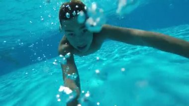 Küçük çocuk sualtı hilariously yüzüyor ve hava slo-mo havuzunda sualtı kabarcıklar ve gökyüzü mavi su olan bir çok çocuk havuzu yüzme mutlu bir çocuk komik bir görünümünü kabarcıklar gönderir. O gözlerini açtı ve neşeli hissediyor