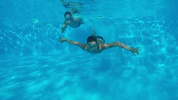 滑稽的男孩在水下游泳在游泳池与天空蓝色水在斯洛伐克 一个乐观坦克射击两个愉快的男孩游泳水下对摄影师和享受生活在一个波光粼粼的蓝色游泳池在慢的运动 — 图库视频影像