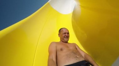 Mutlu adam aqua park tüp üzerinde slaytlar ve elinde bir selfie sopa tutar çekimde heyecan verici bir görüntülemek bir neşeli adam sürgülü dowm sarı Tube aqua park, yaz aylarında. Gülümse ve yavaş hareket selfie sopayla vurur.