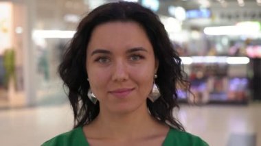 Gülümseyen ve eğlence merkezinde parlak şık genç bir kadın portresi gülümseyen ve onun baş reigh dönüm uzun dalgalı saçlı eğlenirken ve cam gibi bir salonda dururken yaptı neşeli esmer kadın