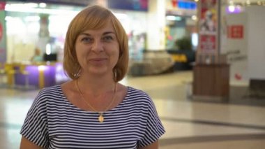 Gülümseyen ve cam gibi bir salonda vitrinler çizgili bir bluz mutlulukla gülümseyerek ve insanlarla bir cam gibi eğlence merkezinde duran bir başarılı ve iyimser sarışın kadın portresi ile ayakta akıllı sarışın kadın 