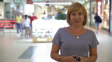 Gülümseyen ve dükkan pencere portre neşeyle gülümseyen ve onu telefon ayakta tutmakla ile geniş bir camsı salonunda çizgili bir bluz içinde şık ve mutlu sarışın kadın ile büyük bir salonda ayakta neşeli sarışın kadın