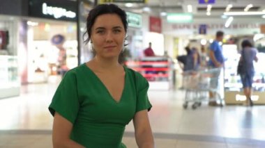 Oturma ve bir vitrinde şık Yeşil elbiseli oturma ve giysileri içinde belgili tanımlık geçmiş ile parlayan bir vitrin ile geniş bir salonda gülümseyen neşeli genç bir kadın portresi zemin ile gülümseyen iyimser esmer kadın