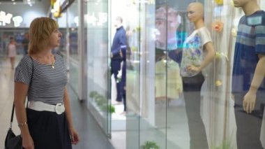Zarif sarışın kadın giysileri bir cam salonda büyük bir dükkanda parlak vitrinler ayakta ve plastik modeller moda giysiler içinde bakarak şık bir sarışın kadın profili yerleştirilir ile vitrin arıyor 