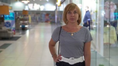 Gülümseyen ve geniş bir salonda vitrinler çizgili bir bluz ve gülümseyen ve cam gibi eğlence merkezinde duran siyah bir etek başarılı ve neşeli sarışın bir kadın portresi ile ayakta emin sarışın kadın