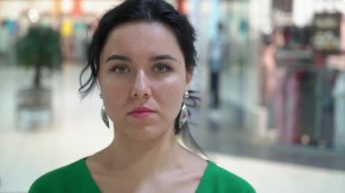 Ayakta ve bir vitrin içinde belgili tanımlık geçmiş moda yeşil giysili ayakta ve giysileri içinde belgili tanımlık geçmiş ile geniş bir salonda bir vitrin ile gülümseyerek mutlu bir genç kadın Closeup ile gülümseyen zarif esmer kadın