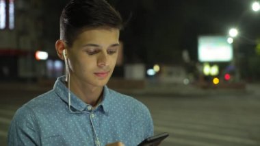 Akıllı genç adam net sörf ve profil müzik ve net metinler kızına sonbahar gece deftere nakil onun smartphone üzerinde tarama sportif bir brunet insanın geceleri ışıklı sokakta duran