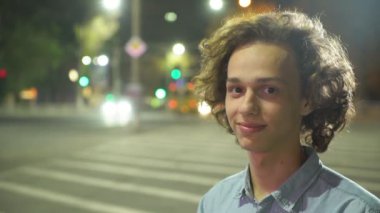 Bir zebra geçiş ayakta ve bir şehirde bir zebra geçiş trafik ile ayakta ve mutlu bir şehirde sokak sonbahar gece gülümseyen uzun dalgalı saçlı Genç bir adam portresi geceleri gülümseyen glamour sarışın adam  