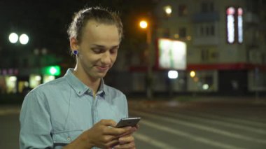 Telefonunu net tarama ve bir sokakta sonbahar profil neşeli bir genç adamın gülümseyen ve onun tatlım rin arayan onun Smartphone'da net sörf bir topuz saç kesimi ile bir sokak sonbahar gece gülümseyen adam düldül