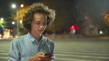 Telefonunu onun tphone üzerinde net sörf ve sonbahar gece fotoğraf onun sevgilim bir sokakta arayan uzun saçlı bir şehirde sonbahar profil romantik bir gencin sokak arasında net tarama aşık genç adam