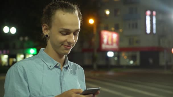 热情的男人在手机上上网 在秋天的一条街道上微笑着简介一个有着魅力耳环的快乐年轻人在手机上浏览网 微笑着在秋天的街道上寻找他可爱的女孩 — 图库视频影像