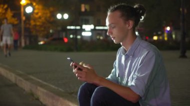 Onun smartphone net tarama ve sonbaharda derin geceleri sokak bir şehirde bilgi isteyen topuz saç kesimi ile sonbahar profil ilham bir gencin sokak bir şehirde oturan yaptığı telefon net sörf Romanticman