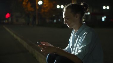 Gülümseyen adam fotoğraf yaptığı telefon smartphone ve yeşil park sonbahar gece derin bilgi arayan neşeli net tarama bir topuz saç kesimi ile sonbahar profil şık bir gencin sokak bir şehirde oturan arayışı