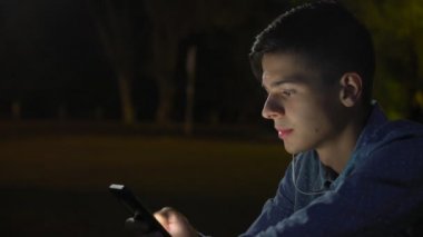 Genç adam onun smartphone üzerinde net sörf ve yeşil park sonbahar gece derin bilgi arayan bir gömlek kısa saçlı sonbahar profil sportif bir brunet adamın bir parkta otururken onun akıllı bilgi arıyor