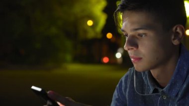 Aşk adam şehir kaldırım kaldırım kenarında oturuyor ve sevgilisine kızıp gece heyecanlı görünümünü romantik bir sportif adam akıllı telefon ekranına bakarak ve onun sevgilim fotoğraf gece arayan kısa saç kesimi ile bakar.