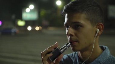Genç adam müzik ve dalgın genç adam bir elektronik sigara ve yoğun bulutlar sonbaharda bir sokakta müzik dinlerken duman dışarı nefes gece bir e-sigara bir sokakta sigara