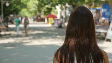 Genç esmer kadın bir yeşil yavaş yaz aylarında sokak boyunca strolling arkadan görünüşü kadar bağsız kıl olan şık bir kadın ve bir yeşil yavaş yaz aylarında güneşli bir sokak boyunca gidiş omuz açık