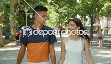 Mutlu çift gülümseyen ve bir yeşil sokak neşeli bir genç adam bir yeşil yavaş yaz aylarında sokak şık uzun saçlı sevimli kız arkadaşıyla portresi slo-mo yaz aylarında yürüyüş aşık