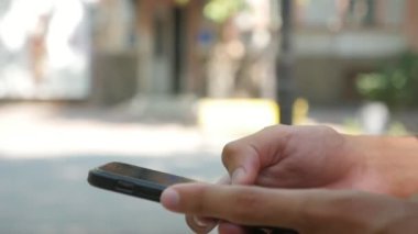 Erkek elinde slo-mo makro atış metinler deftere nakil ve yavaş hareket yaz aylarında güneşli bir günde yeşil bir sokakta modern bir akıllı telefon internette tarama genç erkek el yaz aylarında güneşli bir sokakta getirerek smartphone olduğunu