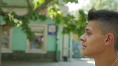 Brunet delikanlı slo-mo profilinde bir kısa saç kesimi ve akıllı eys yavaş yaz aylarında güneşli bir ağaç ve evler bir cadde boyunca gidiş ile sportif bir gencin yaz aylarında yeşil ağaçlar bir sokak boyunca yürüyüş