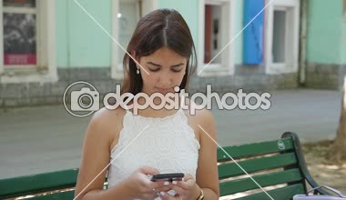 Yaz uzun bağsız kıl ve açık shouldes telefonunu açık havada ağır çekimde yaz aylarında güneşli bir günde internette sörf ile muhteşem bir genç kadının slo-mo profilde bir sokakta telefonunda seyir glamour genç kız