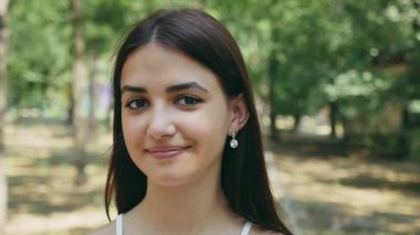 Sevimli genç esmer kadın güneşli bir yaz uzun gevşek esmer saçlı bir neşeli güzel kız mutlu yaz aylarında güneşli çimenler ile yoğun bir orman içinde gülümseyen gözleri parlayan portre bir ormanda gülümsüyor