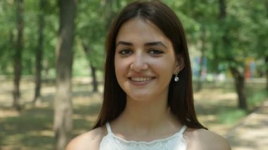 Mutlu genç esmer kadın yaprak bir parkta güneşli bir yaz neşeli bir genç kadının portresi duran ve sonsuza dek mutlu güneşli bir yaz aylarında güneş ışınları dolu yapraklı bir parkta gülümseyen uzun bağsız kıl ile gülümsüyor