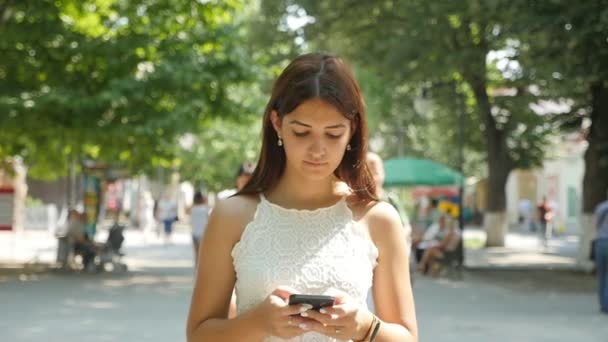 聪明的女人走在小巷里 看着她的手机在夏天在斯洛伐克 莫画像一个美丽的年轻女子与开放的肩膀漫步在一个绿色的小巷 在一个阳光明媚的日子 在夏季慢动作 — 图库视频影像
