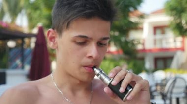 Meditatif genç yavaş hareket e-sigara ve onun burun ve dudakları slo-mo beldesinde yoğun duman dışarı nefes bir entertainign genç adam portresi yaz aylarında bir resort üzerinde bir e-sigara sigara 