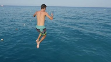 Etkin brunet adam ayak önce denizde ağır çekimde heyecanlı görünümü renkli şort ayak ilk bir iskeleden yaz yavaş dalgalar mavi deniz atlama atletik bir brunet adamın yaz aylarında atlar