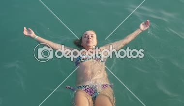 Sırtüstü denizde yaz ağır çekimde kadar renkli bikini deniz sırtındaki forma el ile ağır çekimde yaz aylarında güneşli bir yalan mutlu bir sportif kadın görünümünü aşağı yüzme neşeli sarışın kadın
