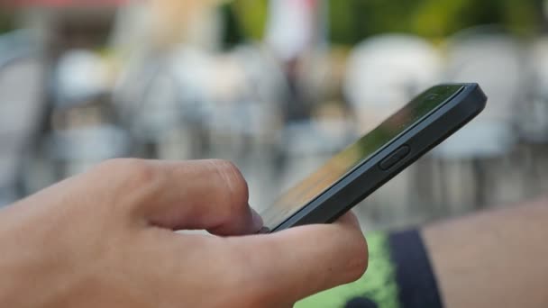 Main masculine surfant sur le net sur un smartphone lors d'une journée ensoleillée en été à Xo@-@ mo Gros plan d'une jeune main masculine naviguant sur le net et cherchant des informations sur un smartphone dans un café lors d'une journée ensoleillée en été au ralenti 