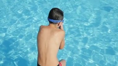 Ayak önce slo-mo Back view on yaşındaki çocuğun ayak ilk şeffaf celeste sularında Yüzme Havuzu su sıçramalarına çok ağır çekimde verme atlama celeste havuza atlama küçük çocuk yüzme gözlüğü