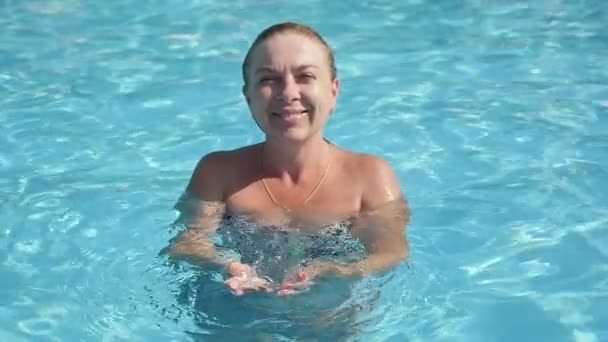 Ayakta ve avuç içi ayakta ve yavaş hareket yaz aylarında aşkın bir yüzme havuzunda su transparan temiz su ile yükselterek neşeli bir sportif kadın portresi yavaş çekimde bir havuzda su yetiştirme mutlu sarışın kadın