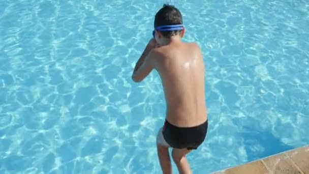 Chlapeček v plavecké brýle skákání nohou nejprve v modré jezírko v zadní zobrazení deset rok starý chlapec potápění nohy první insee-prostřednictvím vody bazénu způsobující spousta bublající postříkání zpomalené slo-mo
