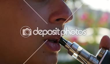 Profili bir adam sigara ve kalın duman e-sigara slo-mo makro atış bir fırt alarak ve onun şık elektronik GAZLAŞTIRICI açık havada ağır çekimde yaz aylarında güneşli bir sigara bir adam üzerinden dışarı nefes