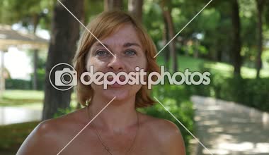 Mutlu yaz aylarında bob saç modeli ve ayakta ve yavaş hareket yaz aylarında yeşil park sokakta neşeli gülümseyen açık omuz ile hoş bir sarışın kadın portresi slo-mo içinde yeşil bir parkta gülümseyen hassas sarışın kadın