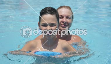 Sarışın Anne ve oğlu yaz slo-mo neşeli mutlu bir anne görünümünü ve gülümseyen oğlunu atlama ve bir yüzme havuzu temiz sularda ağır çekimde yaz aylarında eğlenceli bir swimsaver bir havuzda yüzme ve atlama